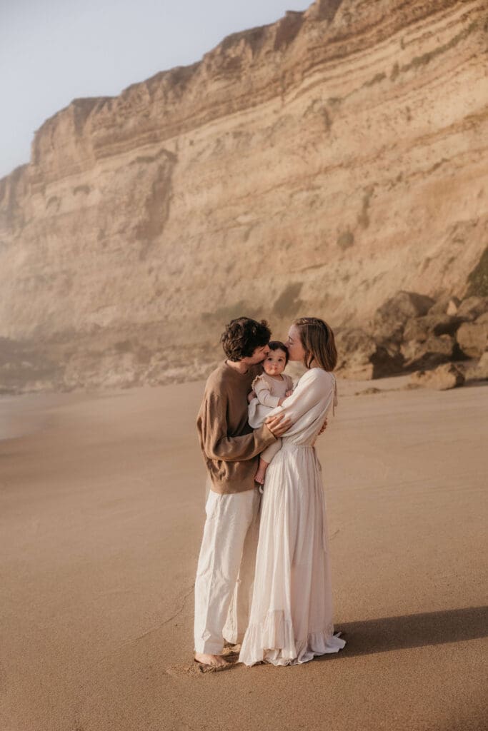 Papa en mama kussen het kind tijdens een fotoshoot op het strand
